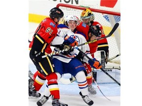 The Edmonton Oliers' Braden Christoffer is checked by the Calgary Flames' Brett Kukak (L) and Ryan Lomberg during an all-rookie game in Penticton, B.C. on Sept. 12, 2015.