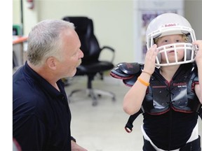 Kelly Hamilton with Regina Minor Football helps 8 year old Braylan Wirth try on a football helmet.