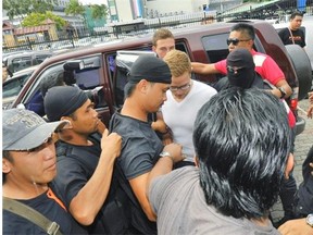 Lindsey Petersen, center, is escorted by police as he arrives at court in Kota Kinabalu, in eastern Sabah state on Borneo island, Malaysia, Friday, June 12, 2015. Petersen was among 10 people who stripped naked and took photos on Mount Kinabalu on May 30. A local official has said the foreignersí behavior caused an earthquake near the mountain last Friday that killed 18 climbers.