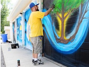 Mural artist Josh Goff works on his mural on a set of garage doors in Regina on Wednesday.