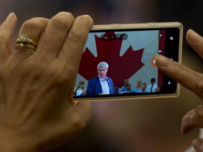 A woman takes a photo of Conservative Leader Stephen Harper as he delivers a speech to supporters during a campaign rally in Toronto on Monday, September 7, 2015.