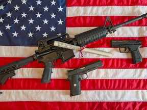 This February 4, 2013 photo illustration in Manassas, Virginia, shows a Colt AR-15 semi-automatic rifle a Colt .45 semi-auto handgun and a Walther PK380 semi-auto handgun and a copy of the US Constitution on top of the American flag.