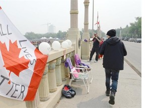 A man walks past a flag and other items memorializing murdered and missing persons on the Albert Street Bridge in Regina on Wednesday July 1, 2015.