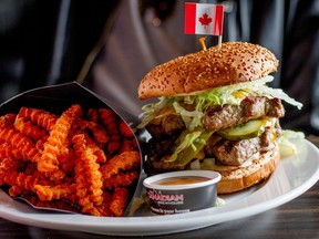 A towering burger at the Canadian Brewhouse with maple leaf shaped beef patties, shredded lettuce, onions, pickles and cheese with yam fries and garnished with a Canadian flag.