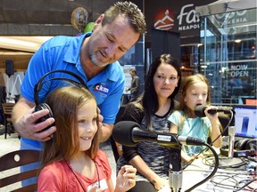 Jamie Lewis, a morning host with CKRM, fits headphones on Myla Moule while her twin sister Morgyn sits with their mom, Jennie, during the Children's Hospital Radiothon which raises funds for the Children's Hospital Foundation of Saskatchewan.
