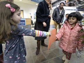 Four-year-old Heam Alarajan (right) accepts a drawing from 4-year-old Juliette Dumont who was at the airport to help welcome about 35 Syrian refugees arriving at the airport Friday evening to round out a total of about 100 throughout the day.
