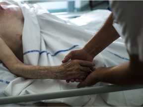 A nurse holding the hand of an elderly patient at the palliative care unit of a hospital.