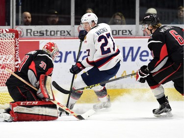 Austin Wagner (C) with the Regina Pats shoots on Moose Jaw Warriors goalie Zach Sawchenko while Warrior, Marc McNulty (R) chases the play during WHL hockey action at the Brandt Centre in Regina on March 11, 2016.