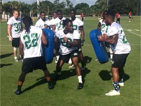 Chevon Walker (26) crashes through tackling dummies held by Paris Cotton (22) and Terrance Cobb (right) during the Saskatchewan Roughriders' mini-camp Monday in Vero Beach, Fla.