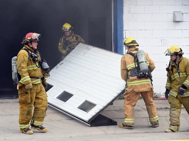 Firefighters take care of a garage door while fighting a fire at Wilf's Autobody & Painting Ltd. on the 1600 block of St. John Street.