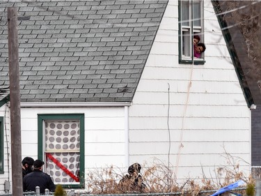 People stick their heads out of a second floor window of a house in the 1100 block of McTavish Street under surveillance by police.