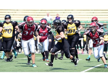 Adrienne Chubala (C) with the Winnipeg Wolfpack runs the ball past member of the Regina Riot during a football game at Mosaic Stadium in Regina.
