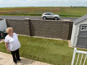 Betty Dooley stands in her backyard while a car drives by on an unpaved section of Pinkie Road in Regina in July.