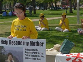Hongyan Lu, left, holds a sign while other Falun Dafa practitioners meditate at Victoria Park in Regina, Sask. on Monday July 25, 2016. Lu's mother Huixia Chen was abducted by the Chinese government on June 3rd of this year.
