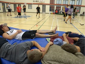 Tanner Kozun, left, sleeps while others continue playing floor hockey in the École Monseigneur de Laval gymnasium in Regina, all part of an indie film that is aiming for the world record for longest floor hockey game.