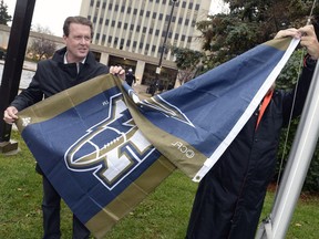 Mayor Michael Fougere raises a Winnipeg Blue Bombers flag in front of City Hall.