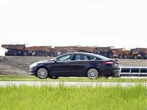 A car passes heavy duty road construction equipment atop some of the already completed Regina Bypass.