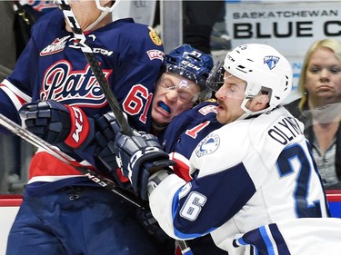 Kolten Olynek (R) with the Saskatoon Blades hammers Austin Wagner (C) with the Regina Pats as he pushes him into fellow Pat,  Filip Ahl (L) during a Western Hockey League game at the Brandt Centre in Regina.