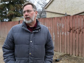 Charles Kooger stands beside some spray-painted racist remarks in the alley near his house.