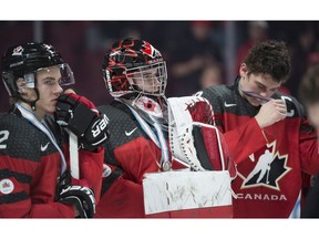 Canada's Jake Bean and Carter Hart stand with silver medals around their neck as captain Dylan Strome removes his after losing to the United States at the IIHF world junior championship on Thursday.