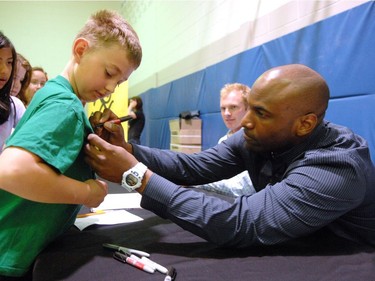 Alex Harris (L) 9 years in grade four at St. Francis Community School has his Riders t-shirt autographed by Saskatchewan Roughriders QB Darian Durant (R) during the kick-off to KidSport Month in Regina on May 04, 2011.