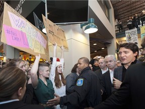 Two women hold protest signs referring to the Dakota Access and Kinder Morgan Trans Mountain oil pipeline projects as Prime Minister Justin Trudeau makes his way through the crowds at the University of Regina on Jan. 26, 2017.