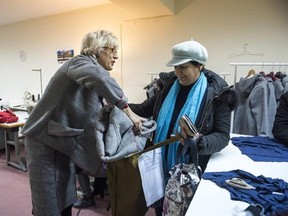 In this Monday, Jan. 30, 2017, project organizer Elke Wollschlagerr from Germany, left, gives a jacket made from a blanket to a Greek woman, at a tiny workshop charity called Naomi in the northern Greek city of Thessaloniki, which is working long hours to collect and wash discarded blankets and turn them into wearable coats. The blankets are mostly army issue gray with red stitching and are distributed as aid at the sprawling refugee and migrant encampments, and are being recycled into practical
