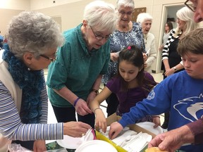 Norma Frizzell (L) grabs some cutlery with Alexis Mohr-Bundus (R) at a potluck lunch at Bulyea Elementary School in Bulyea, Sask. on Friday, Mar. 11. The potluck was a warp up to a pen pal program that the Grade 4, 5 and 6 class had been doing with seniors in the community. PHOTO ASHLEY ROBINSON
