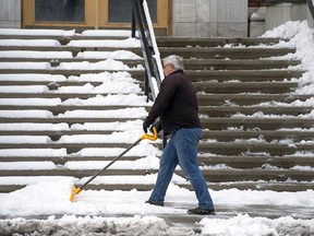 A worker clears snow from the sidewalk in front of the Saskatchewan Sports Hall of Fame.