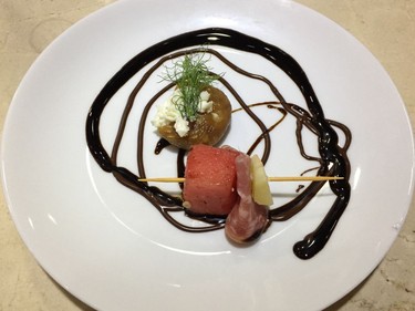 A charcuterie plate featuring a stuffed fig and a skewer with watermelon, salami and manchego, drizzled in semisweet chocolate.