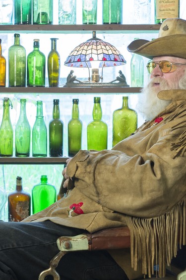 WHITEWOOD, SASK : June 15, 2017 - George Chopping sits in a barber chair, in the window a small part of his bottle collection at Old George's Museum and Hidden Village. MICHAEL BELL / Regina Leader-Post.  Through active involvement in the collecting community, Chopping became something of an expert on prairie bottles. He spent years at Beausejour at the site of Manitoba Glass Works collecting, and self-published a book called Bottles of the Canadian Prairies.