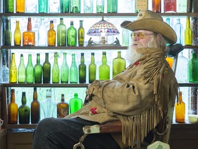 George Chopping sits in a barber chair, in the window a small part of his bottle collection at Old George's Museum and Hidden Village.