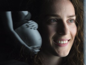 Andreea Tamaian, a doctoral student in clinical psychology, is seen through glass that reflects a picture of a pregnant woman illuminated by a computer screen at the University of Regina.