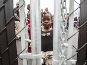 This file photo taken on August 5, 2017 shows a girl who crossed the Canada/U.S. border illegally with her family, claiming refugee status in Canada, as she looks through a fence at a temporary detention centre in Blackpool, Que.