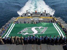 Sailor pack the helicopter pad of the frigate HMCS Regina to see a giant battle ensign saluting the Saskatchewan Roughriders.