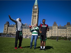 Roughriders fan Donna Kitchen, flanked by receivers Bakari Grant, left, and Caleb Holley, caught a pass Sunday when the team practised on Parliament Hill.