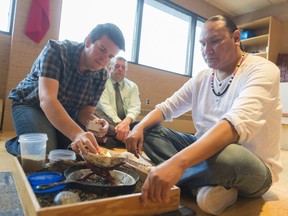 Paul Cutting (left) lights some sage while assisting Terrance Littletent in a smudge ceremony, while director of education Greg Enion (centre) looks on at the Regina Public School Division office.