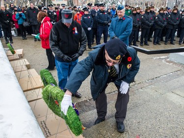 A man bends down to pick up a wreath to lay at the foot of the cenotaph during the Remembrance Day service in Victoria Park.