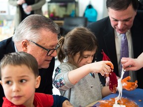Federal Minister of Public Safety Ralph Goodale, leaning in from left, and Saskatchewan deputy premier Gord Wyant, right, watch as Bridget McMurray, in grey, and Severn Kramer-Cadenne, in red, do a craft with glue at the Seven Stones Child Care Centre in Regina.