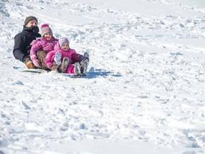 Dan Drackett, left, and his daughters, two-year-old Hazel, right, and four-year-old Stella, centre, ride down a hill on a toboggan at Pascoe Park in the Crescents neighbourhood in Regina.