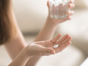 Close up photo of one round white pill in young female hand. Woman takes medicines with glass of water. Daily norm of vitamins, effective drugs, modern pharmacy for body and mental health concept