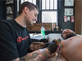 Jesse Exner, left, tattoos Greg Elkington at the Blacksmith Art Studio on Halifax Street in Regina.