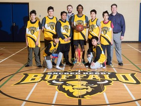 The boys basketball team from Sacred Heart Community School stand together in the school's gymnasium. Front row on knees, left to right: John Nepomuceno, Nguyen Cao. Standing, left to right: Frankie Clampitt, Dettrius La Rose, Jomel Bacor, Victoire Tumba, Jalen Funmaker, Legacy Kahnapace .Coaches – Dan Koskie, left, and Dave Magnusson.