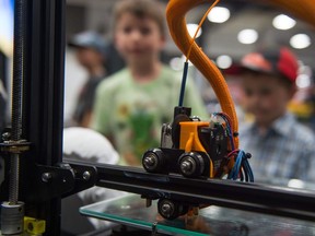 John Delorme, right, and Ethan Delorme look at a 3D printer on display at Canada's Farm Progress Show at Evraz Place.