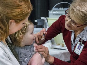 Tara Anderson holds her daughter Charlotte while receiving a flu vaccine from public health nurse Joan Kirkpatrick during opening day of flu shot season at Prairieland Park, October 21, 2015.