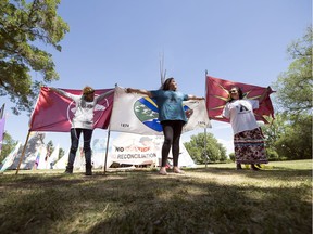 Three people stand with flags after an announcement made at the Justice for Our Stolen Children protest camp in Wascana Centre in Regina.