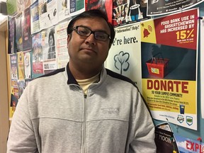 Hammad Ali is a graduate student at the University of Regina who uses the URSU Cares Pantry program, which supplements students' food and household needs in partnership with the Regina Food Bank. He stands next to a poster seeking food bank donations in the Riddell Centre.