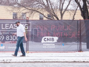 A man walks past a section of vandalized fencing surrounding property near the intersection of Broad Street and Broadway Avenue. The graffiti appeared to stem from ongoing local tension over development in Wascana Park, which has sparked a series of public protests. Some of the graffiti appeared to target the company Brandt, which intends to erect a building, to include a new CNIB office, at the location.