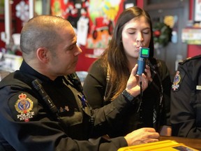Cst. Marcus Simons with the Regina Police Service demonstrates how to use a roadside alcohol breath tester on volunteer Jennifer Sully, communications officer for SGI during an event to address impaired driving put on by SGI on Dec. 28, 2017.