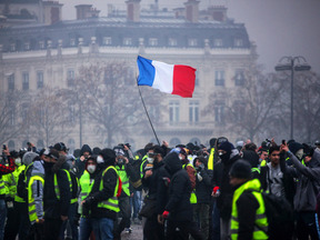 Demonstrators gather under a French flag near the Arc de Triomphe during a protest of "gilets jaunes" (yellow vests) against rising oil prices and living costs, Dec. 1, 2018 in Paris.